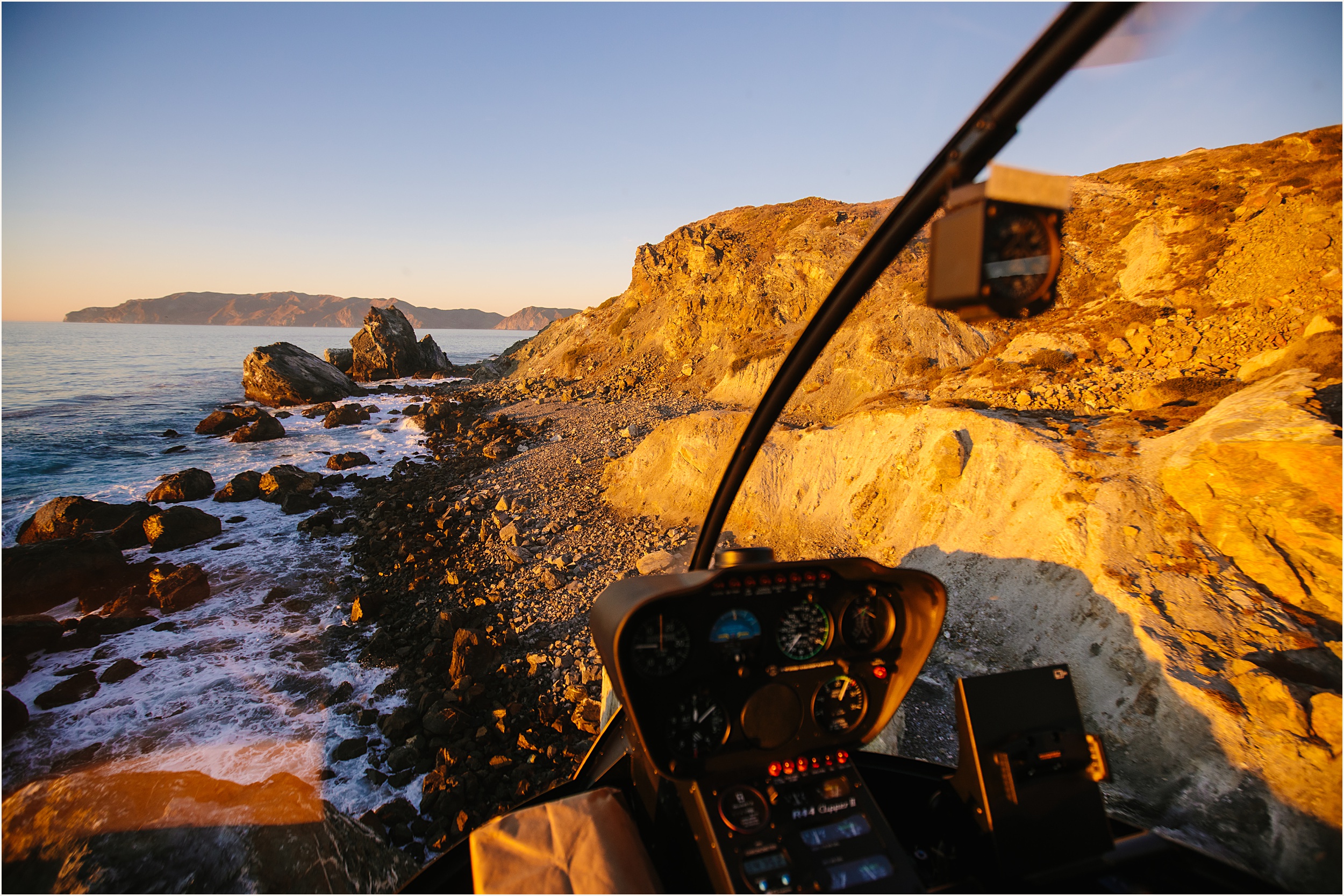 photo of a view from inside a helicopter looking at ocean and a cliffside