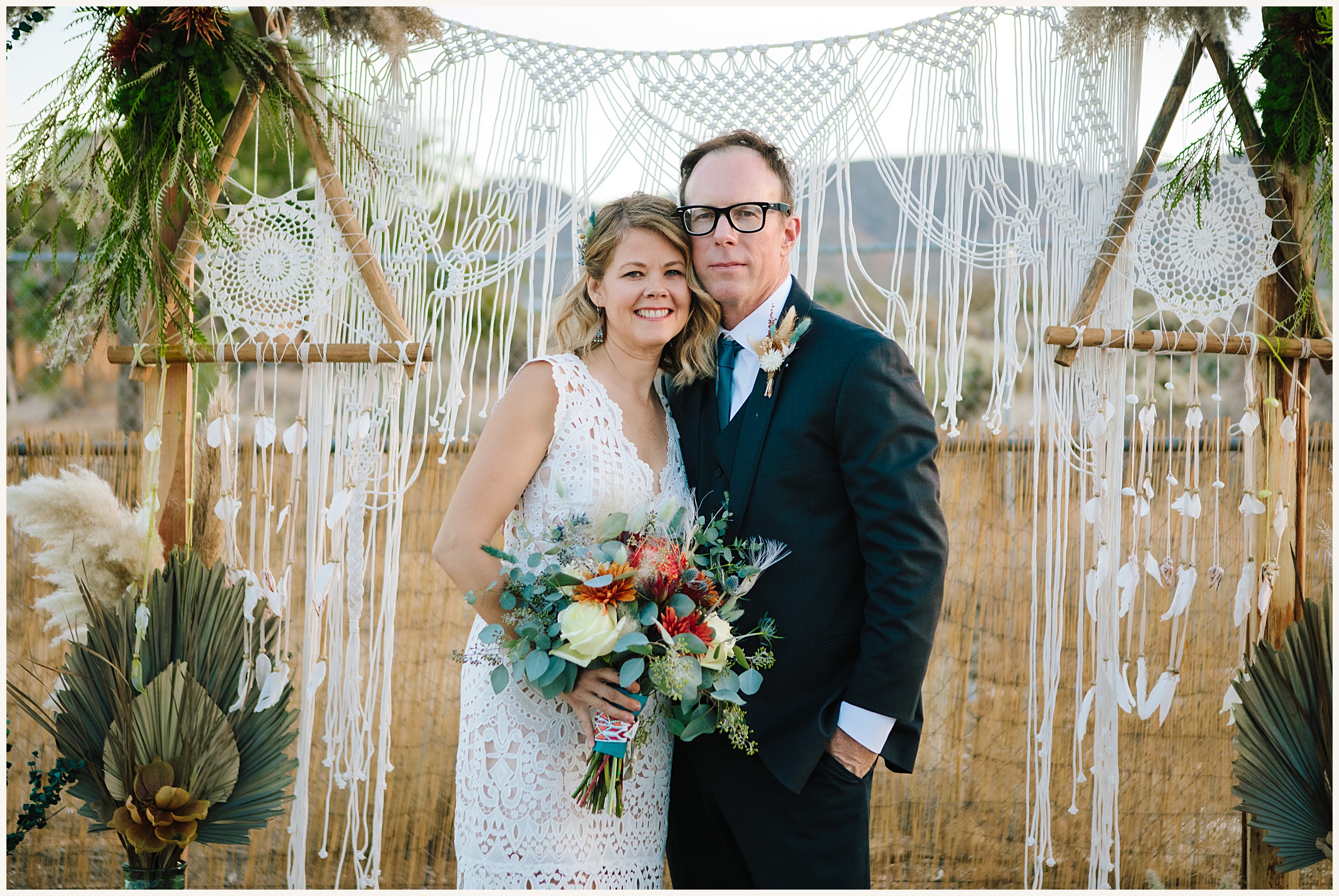 Photo of bride and groom in front of bohemian wooden arch bohemian macrame hanging after Joshua Tree elopement ceremony
