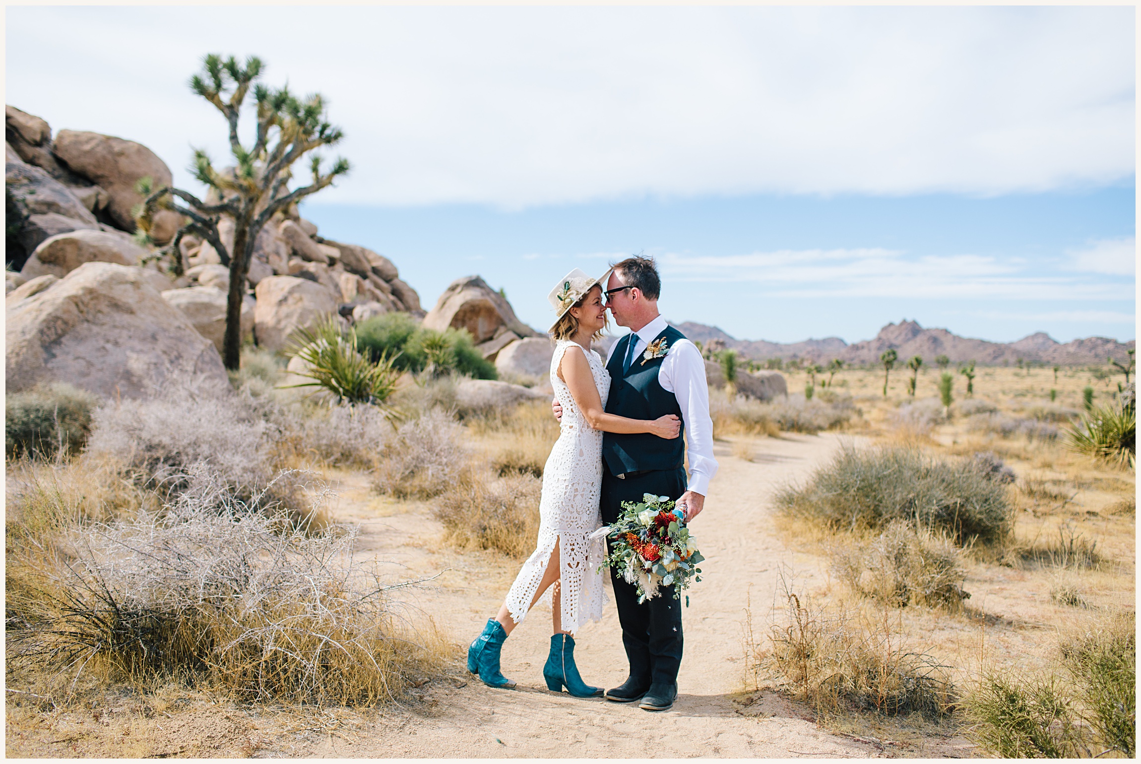 Photo of bride wearing an elegant white lace A-line elopement dress and groom wearing a black wedding suit and white button up in Joshua tree