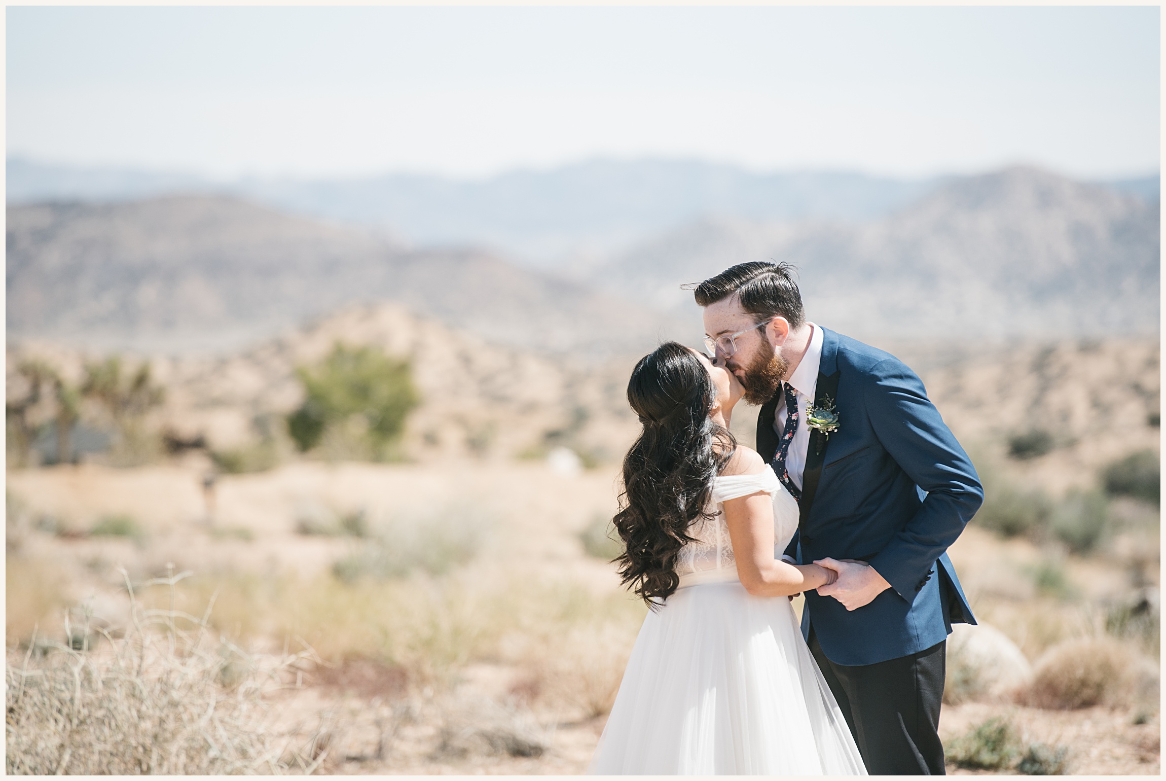 Photo of bride and groom kissing, bride wearing off the shoulder white elopement dress and groom wearing a blue wedding suit