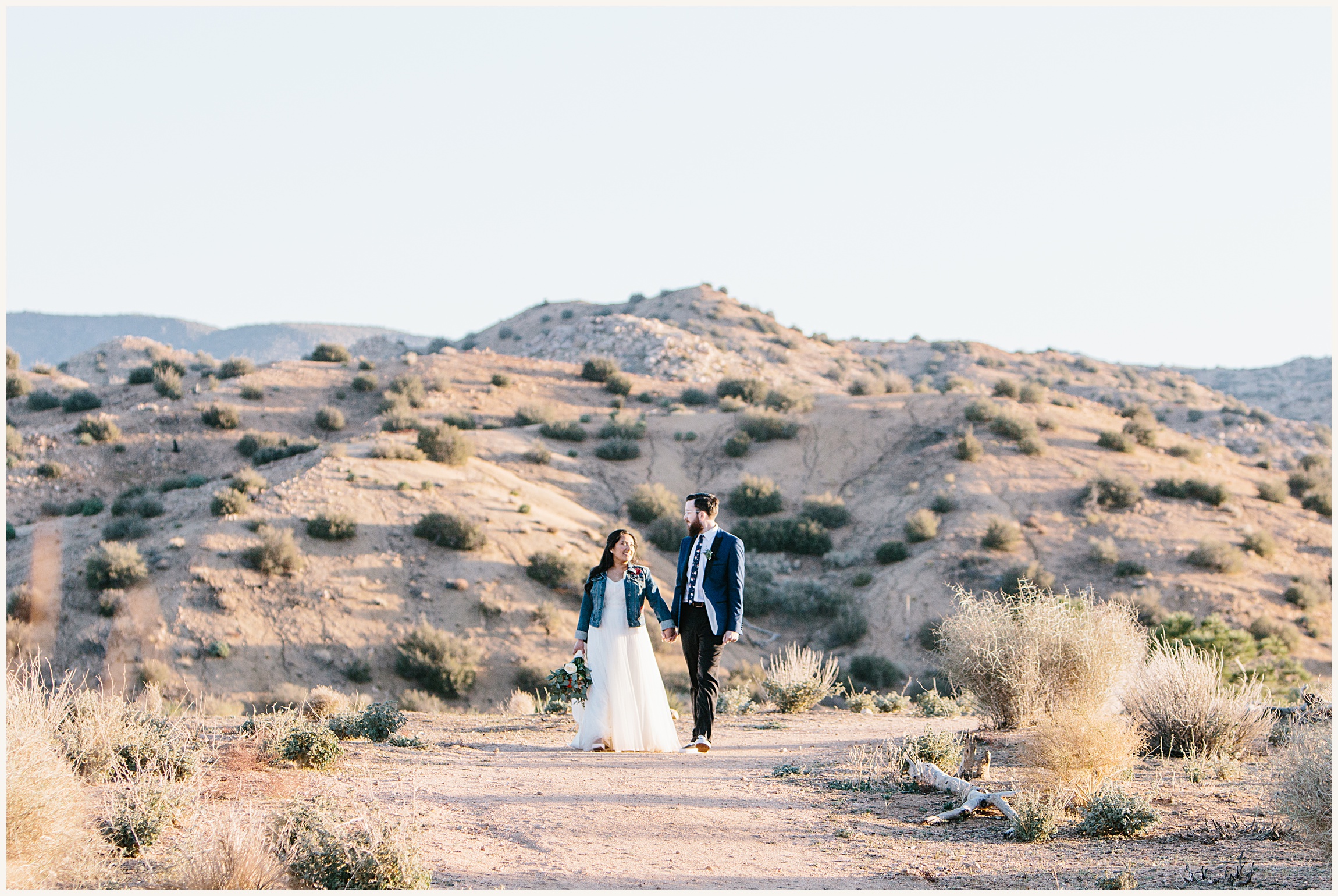 Photo of bride wearing off the shoulder white elopement dress with a jean jacket and groom wearing a blue wedding suit