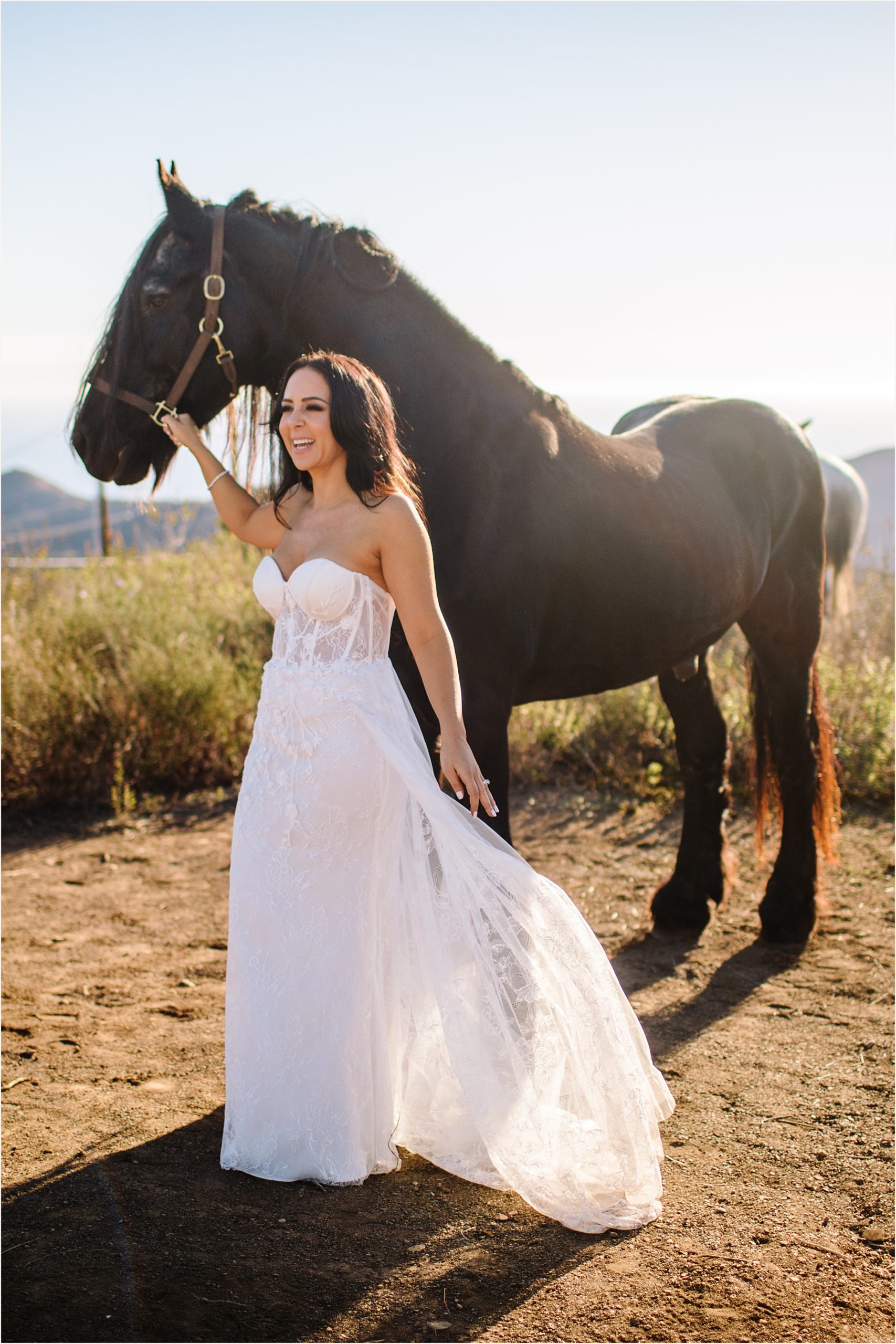 Photo of bride holding onto brown horses harness and laughing