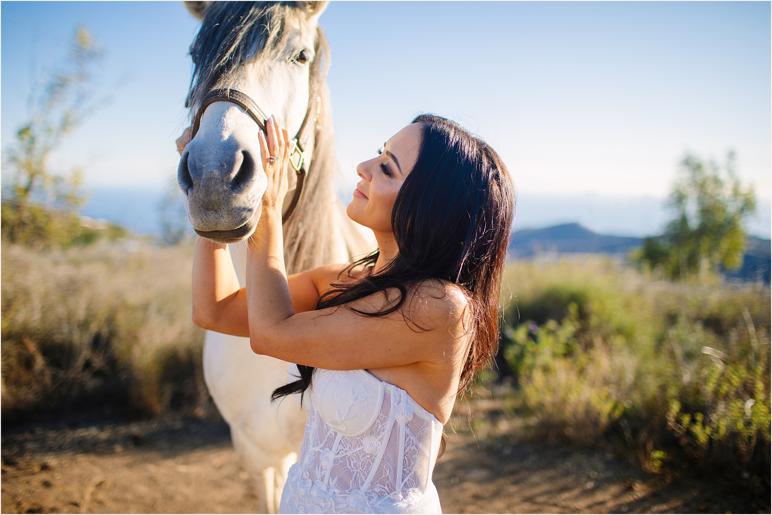 Photo of bride petting a white horse in strapless lace mermaid elopement dress