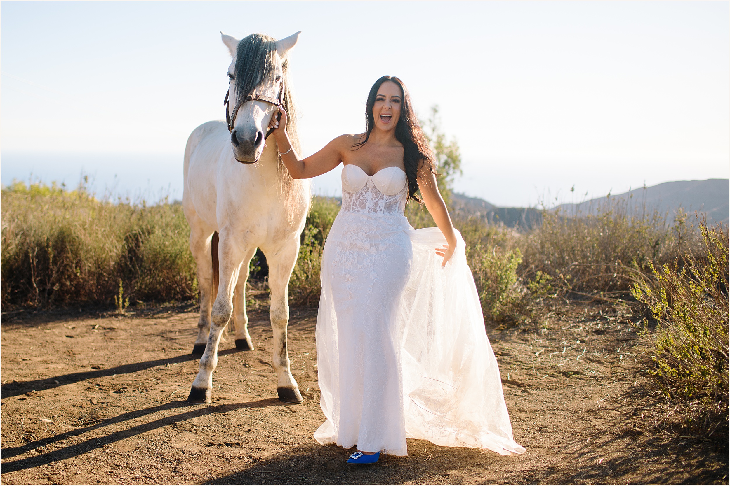 Photo of bride holding onto white horses harness and laughing