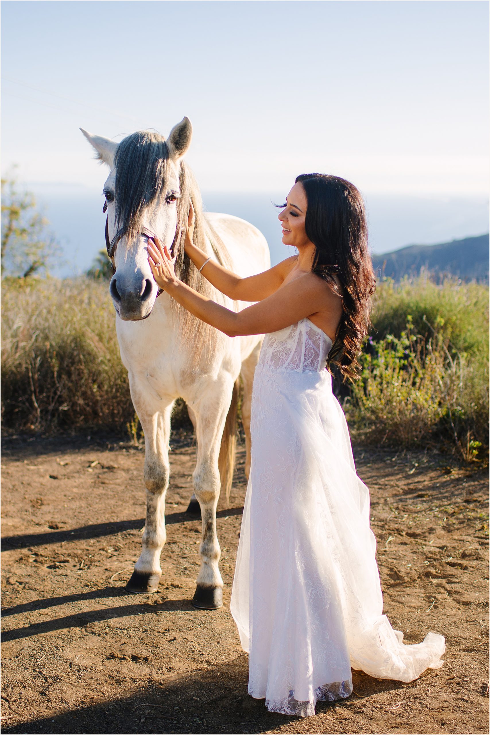 Photo of bride in strapless mermaid dress petting a beautiful white horse