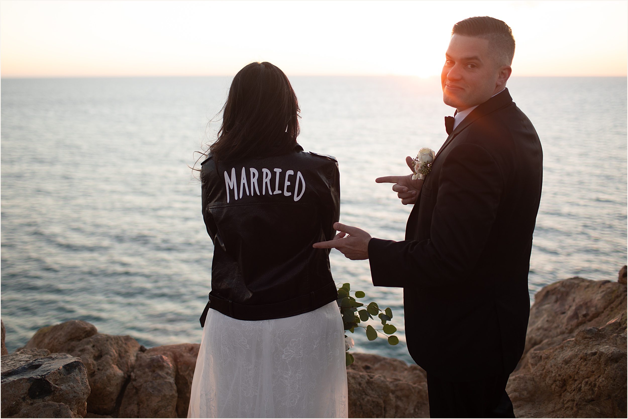 Photo of groom pointing at brides wedding leather jacket that reads Married on the back during their Malibu beach elopement