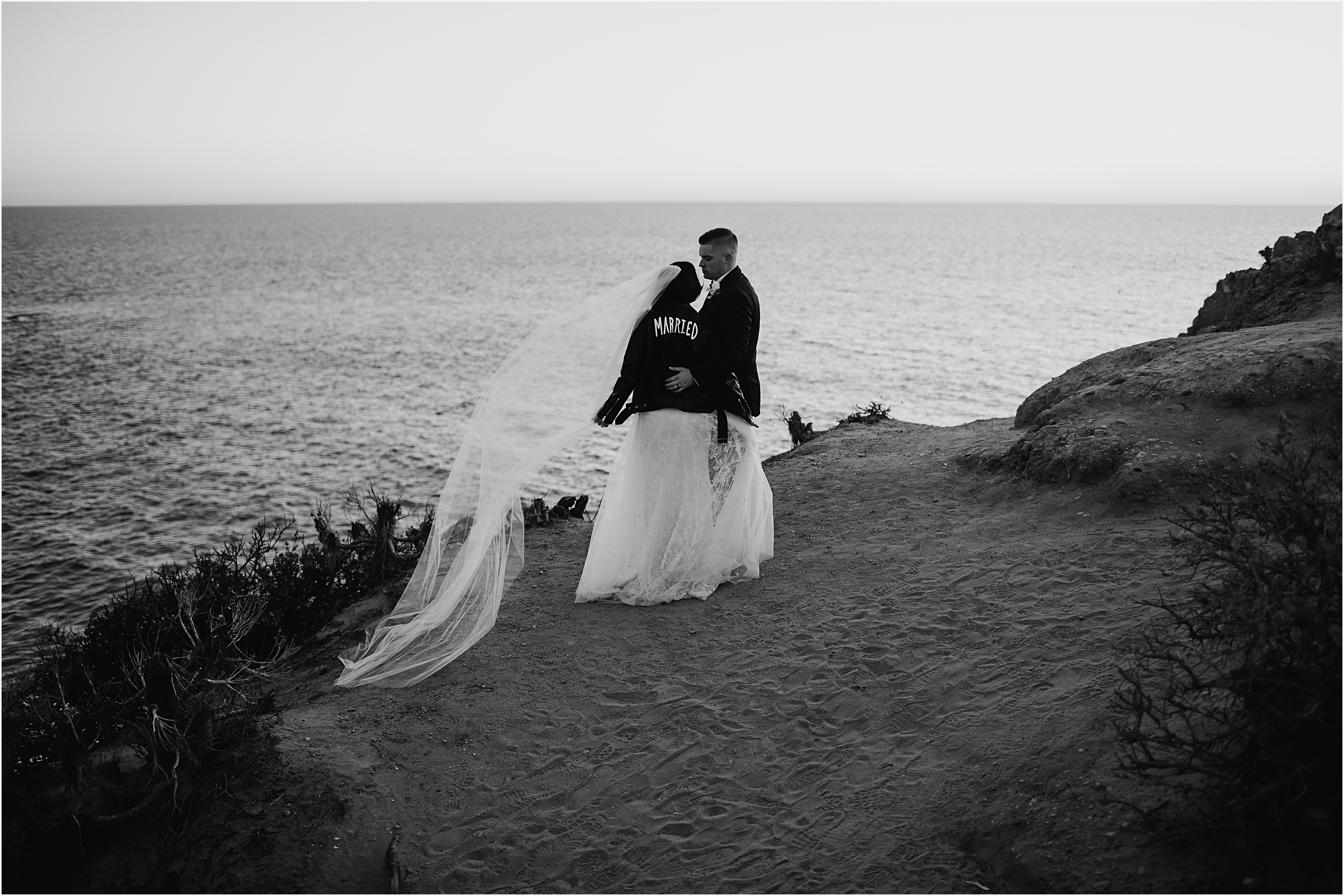 Black and white photo of bride and groom on cliffside view looking at one another during their Malibu beach elopement