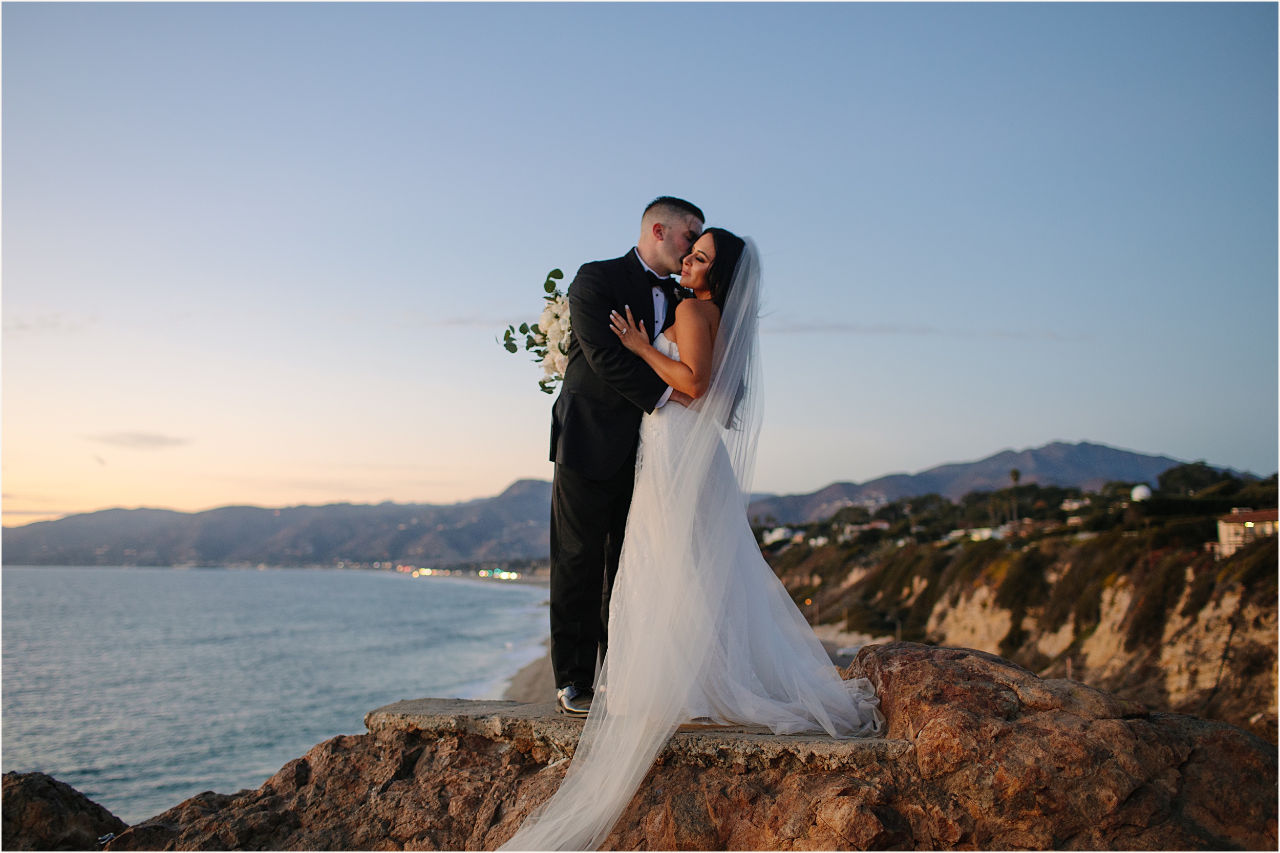 Photo of bride and groom embracing one another on cliffside view during sunset for their Malibu beach elopement 