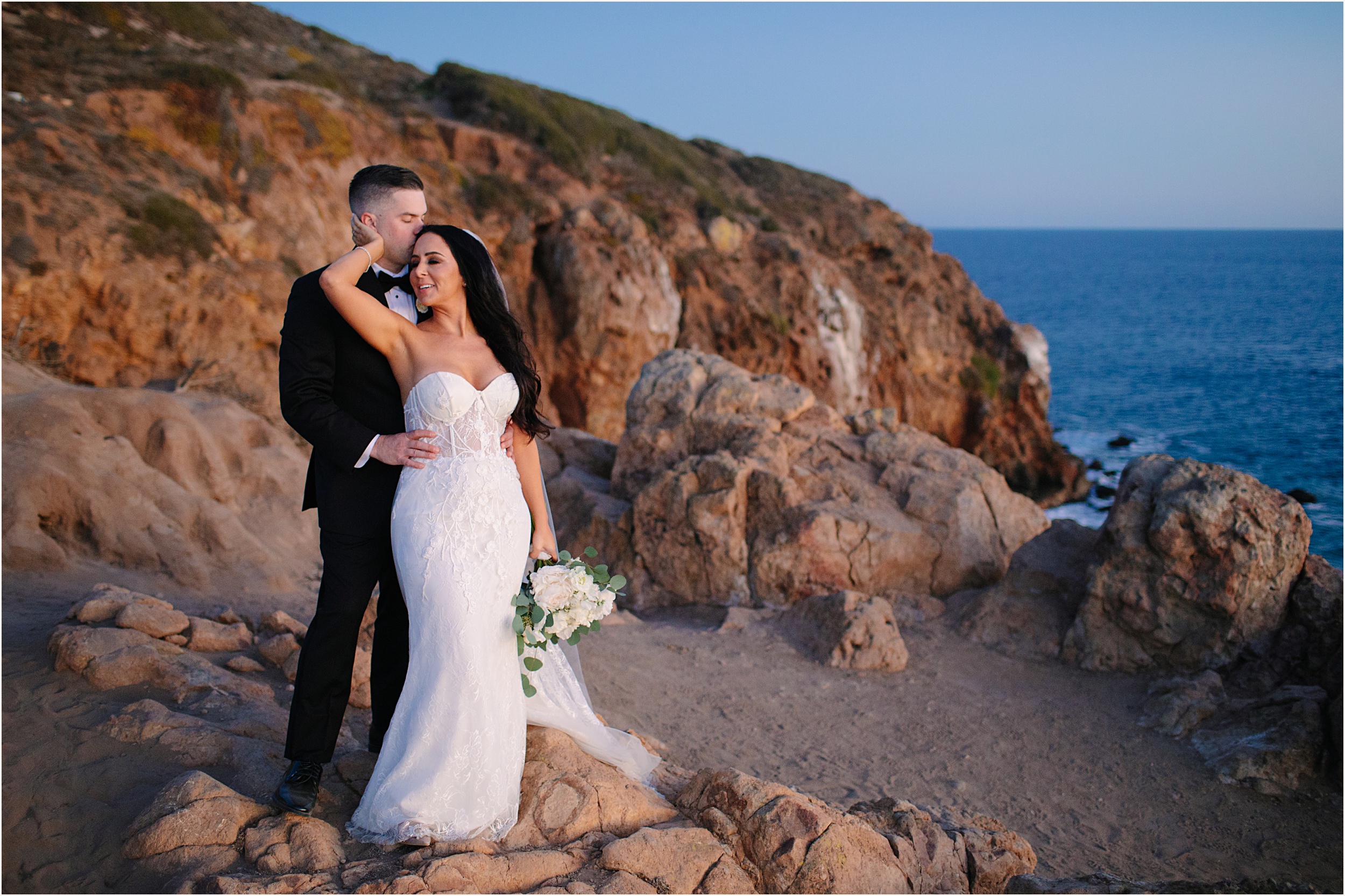 Photo of bride and groom embracing one another on cliffside view during sunset during their Malibu beach elopement