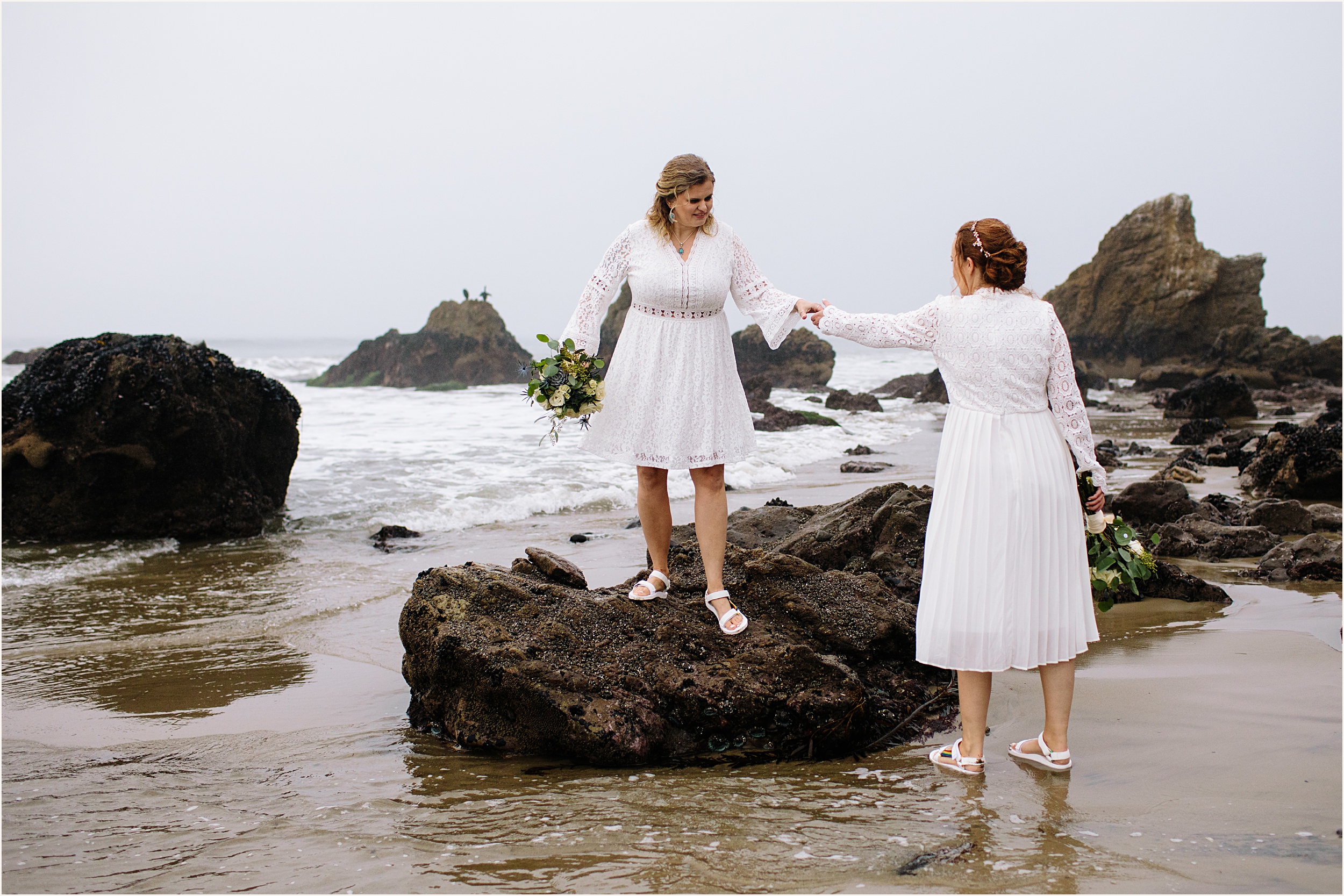 Photo of brides in stunning white lace elopement dresses at El Matador beach climbing rocks