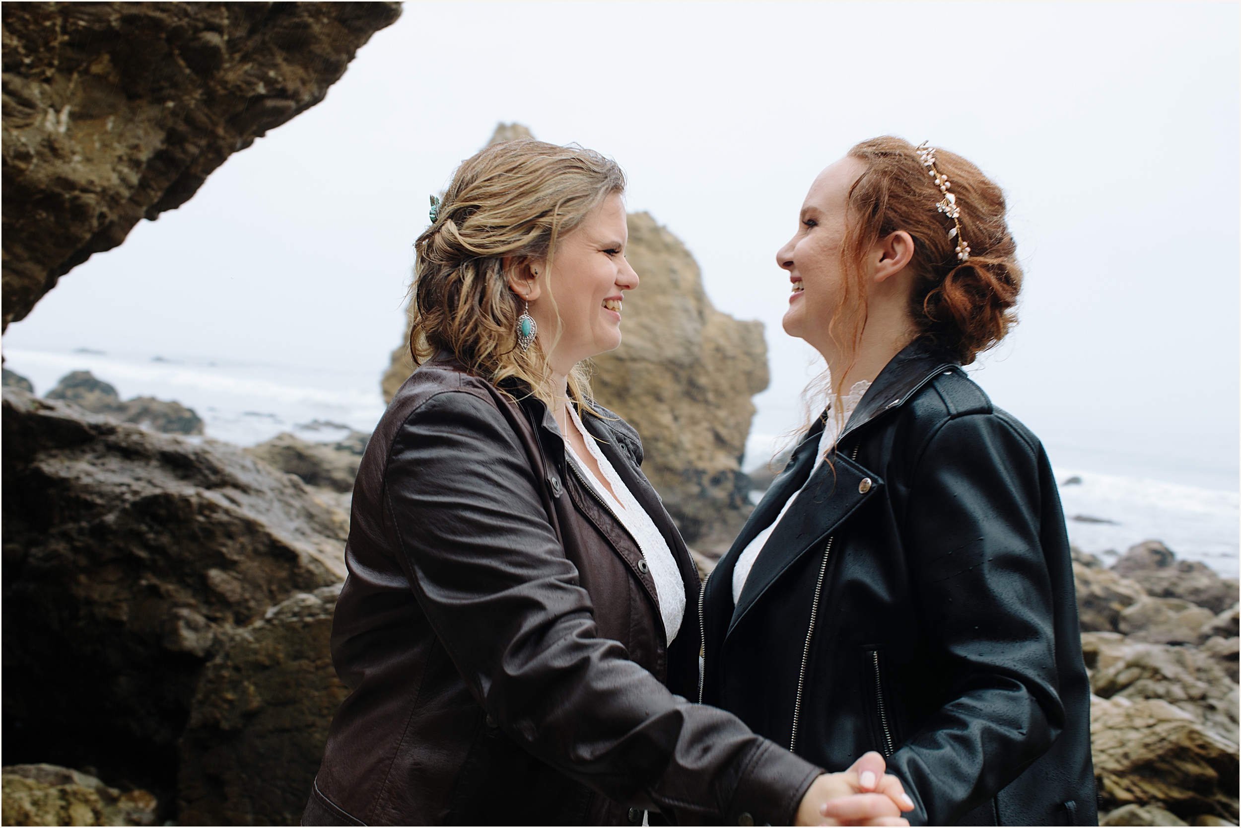 Photo of brides in leather jackets facing eachother laughing at El Matador beach