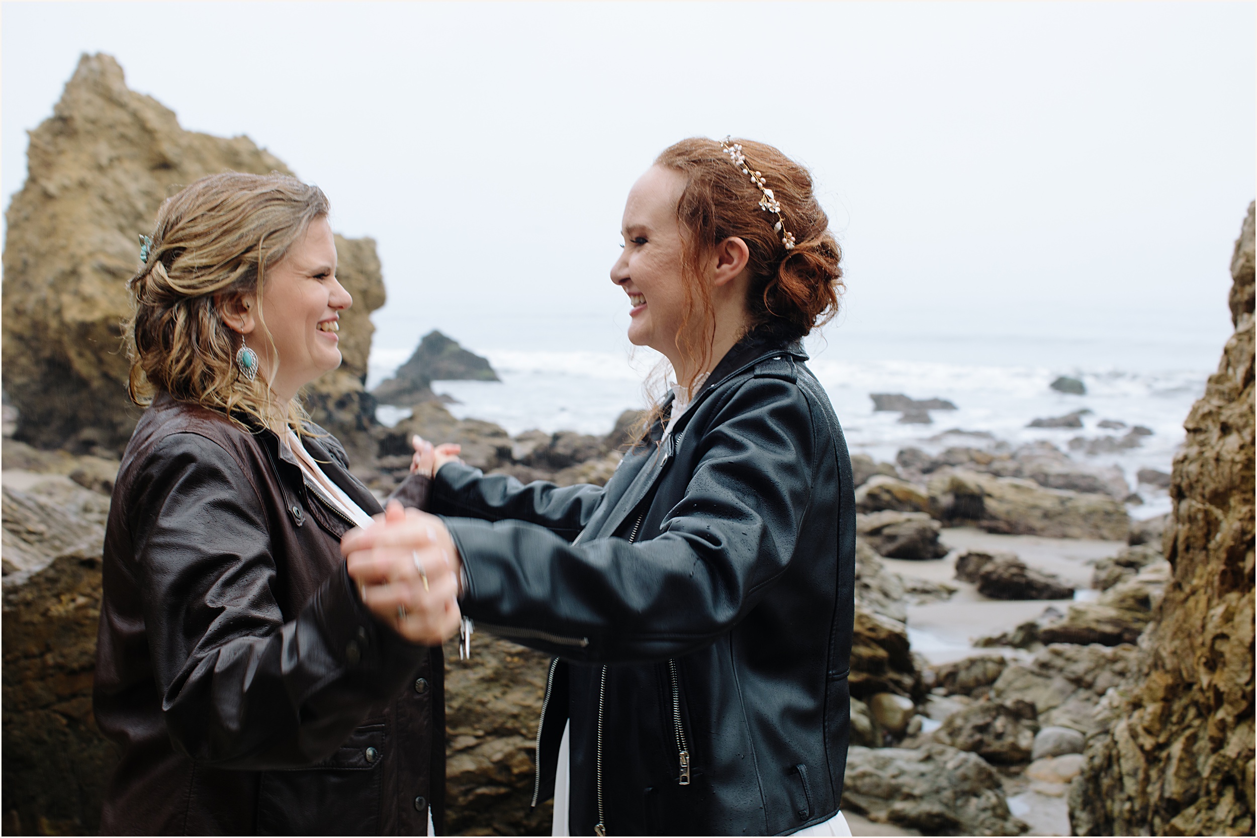 Photo of brides in leather jackets facing eachother laughing at El Matador beach