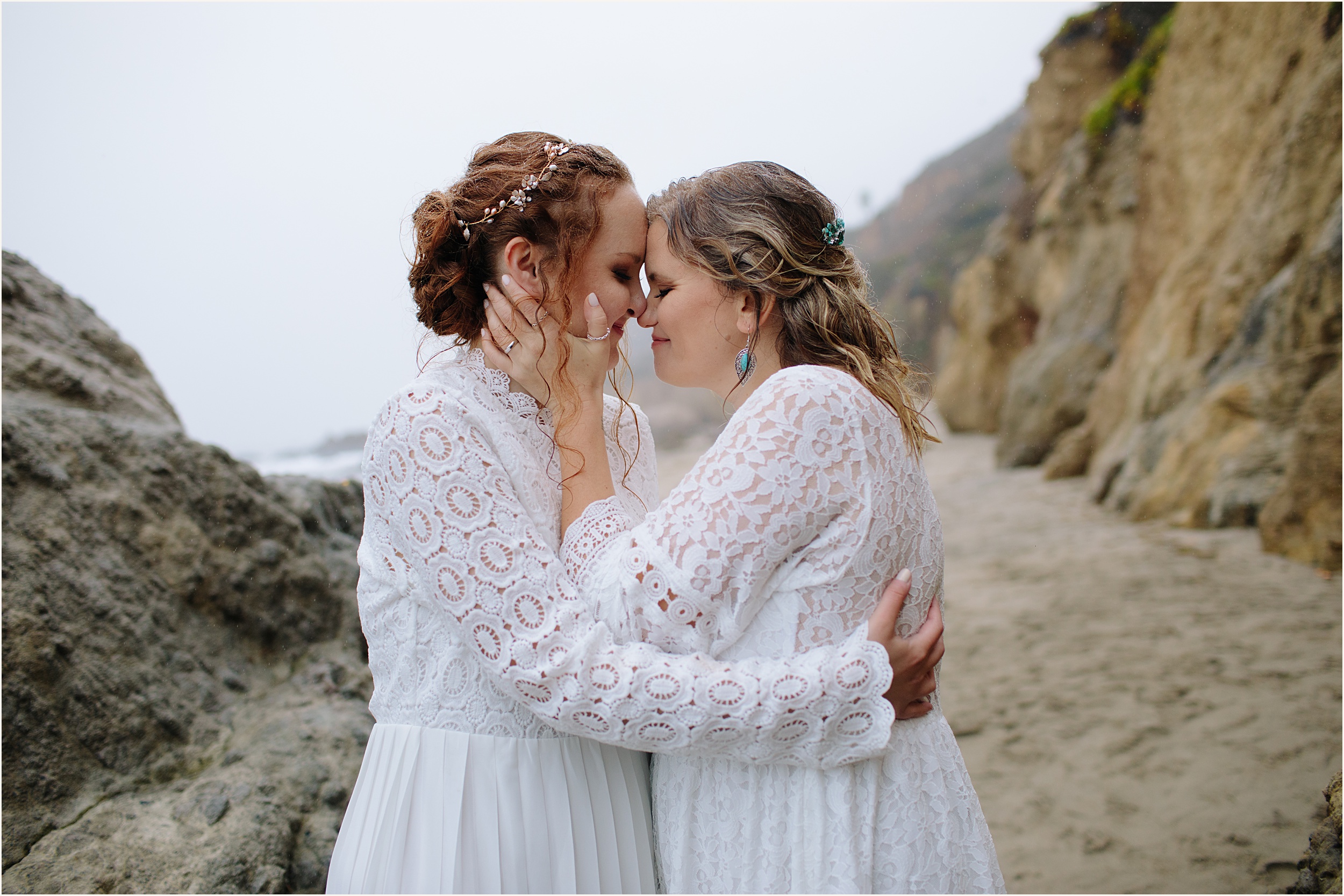 Photo of brides facing and holding eachother in stunning white lace elopement dresses at El Matador beach